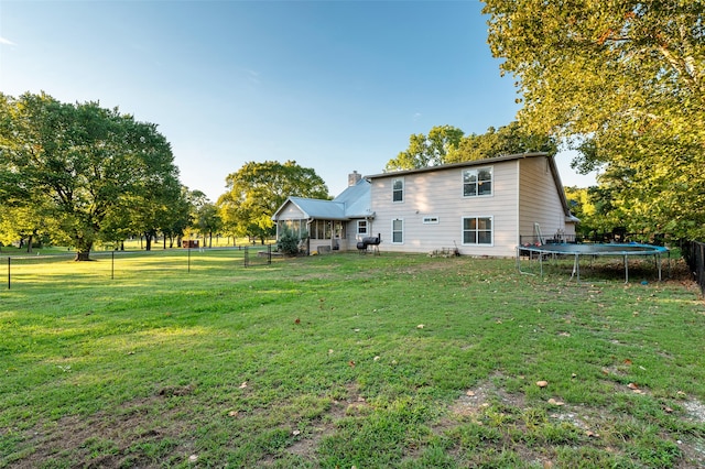 back of house featuring a sunroom, a trampoline, and a yard