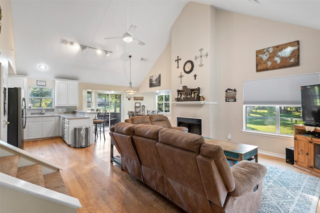 living room featuring ceiling fan, high vaulted ceiling, and light hardwood / wood-style flooring