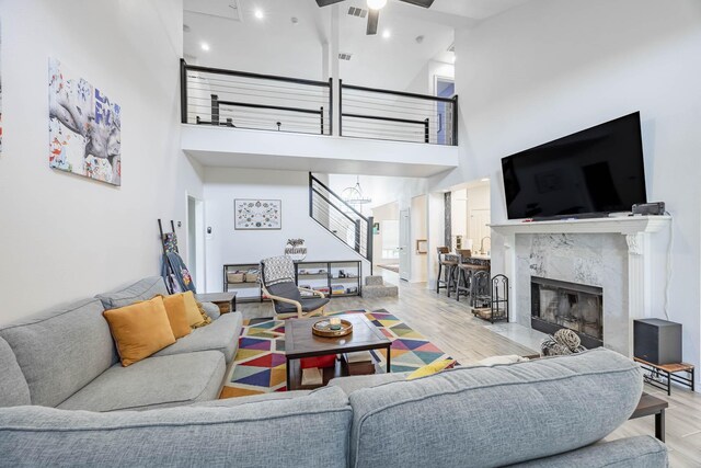 living room with light wood-type flooring, ceiling fan, a premium fireplace, and a towering ceiling