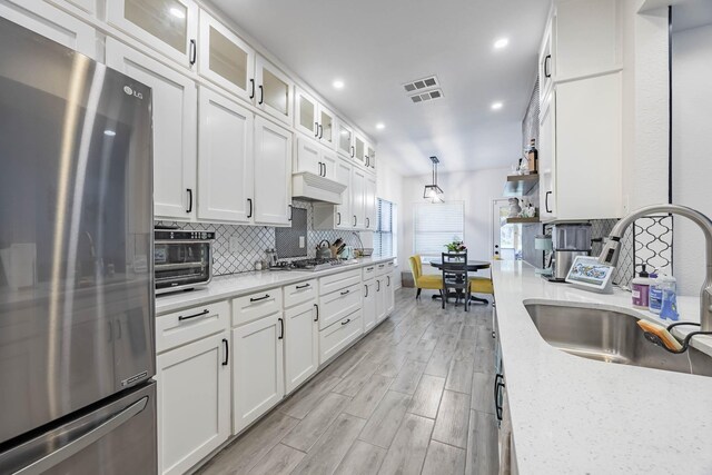 kitchen featuring light wood-type flooring, white cabinetry, sink, light stone countertops, and appliances with stainless steel finishes