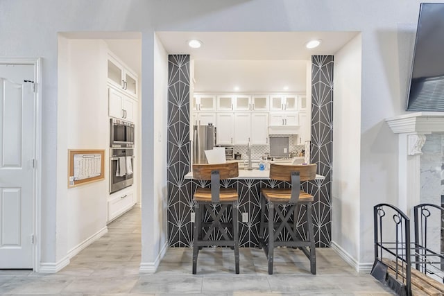 kitchen featuring stainless steel appliances, tasteful backsplash, glass insert cabinets, white cabinets, and a kitchen breakfast bar