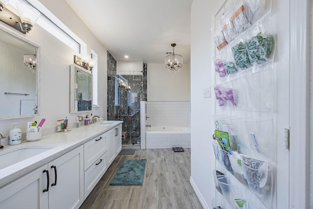 bathroom with wood finished floors, a sink, a bath, double vanity, and a stall shower