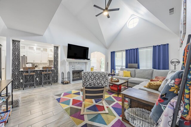 living room with ceiling fan, a high end fireplace, high vaulted ceiling, and light hardwood / wood-style floors