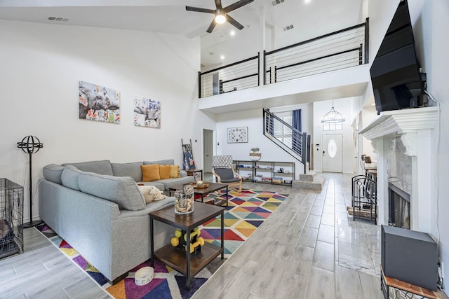 living room with ceiling fan, a high ceiling, visible vents, stairs, and wood tiled floor