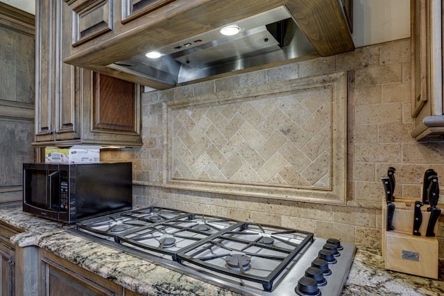 kitchen with decorative backsplash, light stone countertops, custom range hood, and stainless steel gas cooktop