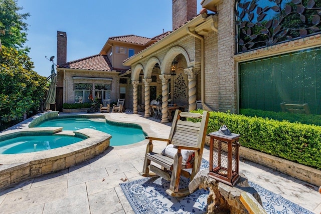 rear view of property featuring a patio area and a pool with hot tub