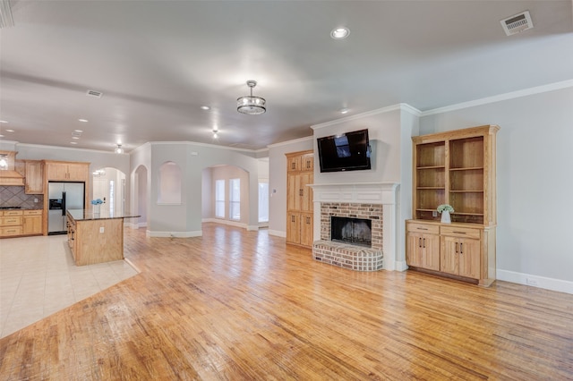 unfurnished living room with light hardwood / wood-style flooring, crown molding, a notable chandelier, and a brick fireplace