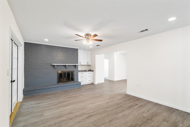 unfurnished living room with ceiling fan, a brick fireplace, and light wood-type flooring