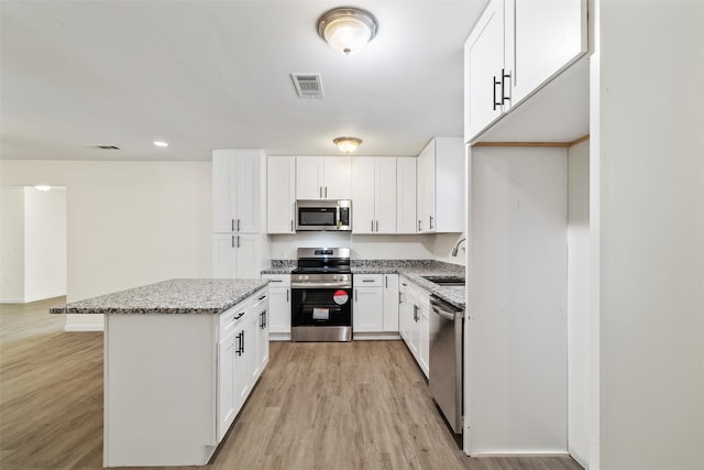 kitchen with white cabinetry, stainless steel appliances, light stone counters, and light wood-type flooring