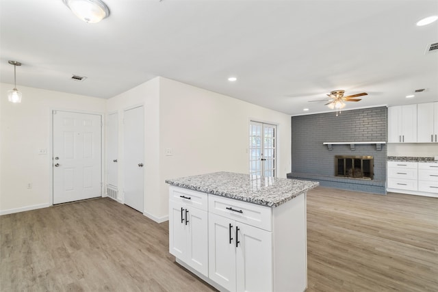 kitchen featuring a fireplace, decorative light fixtures, white cabinets, light stone countertops, and light hardwood / wood-style flooring