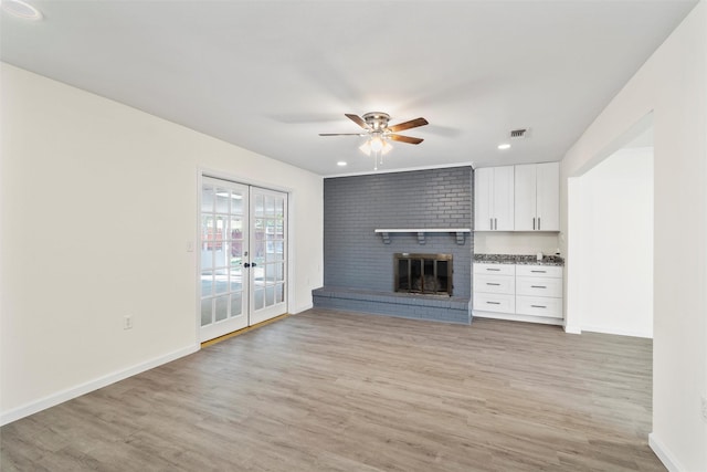 unfurnished living room with ceiling fan, a fireplace, light hardwood / wood-style floors, and french doors