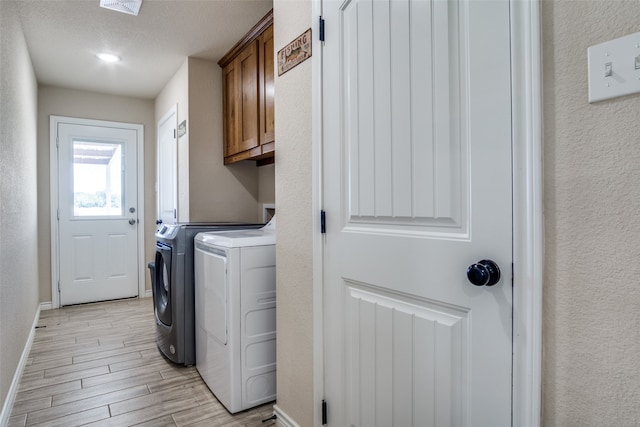 laundry area with light wood-type flooring, a textured ceiling, cabinets, and washing machine and dryer