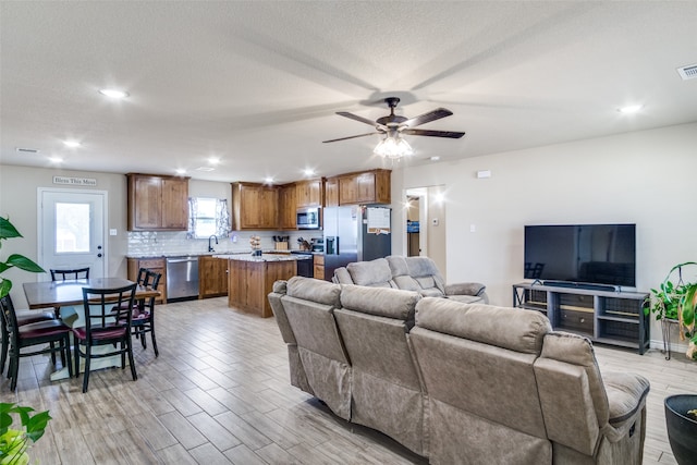 living room featuring ceiling fan, light hardwood / wood-style floors, a textured ceiling, and sink