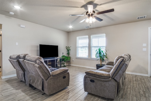 living room with a textured ceiling, light hardwood / wood-style flooring, and ceiling fan