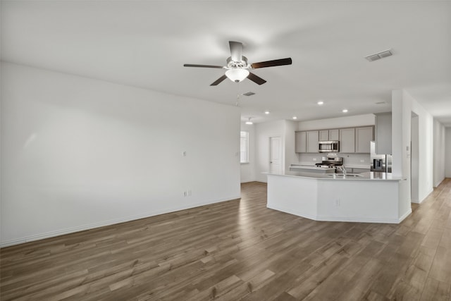 kitchen featuring hardwood / wood-style flooring, appliances with stainless steel finishes, gray cabinets, an island with sink, and ceiling fan