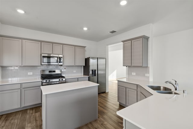 kitchen with stainless steel appliances, sink, gray cabinets, dark wood-type flooring, and a kitchen island