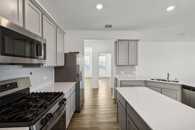 kitchen with hardwood / wood-style floors, tasteful backsplash, stainless steel appliances, sink, and gray cabinets