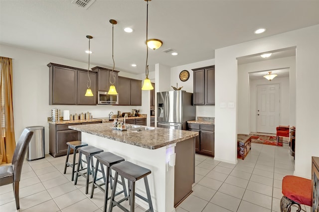 kitchen featuring decorative light fixtures, appliances with stainless steel finishes, an island with sink, a breakfast bar, and light stone counters