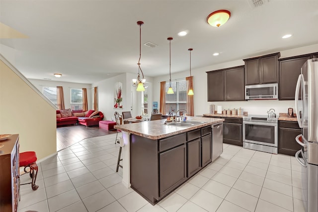 kitchen with decorative light fixtures, stainless steel appliances, light hardwood / wood-style floors, sink, and a center island with sink