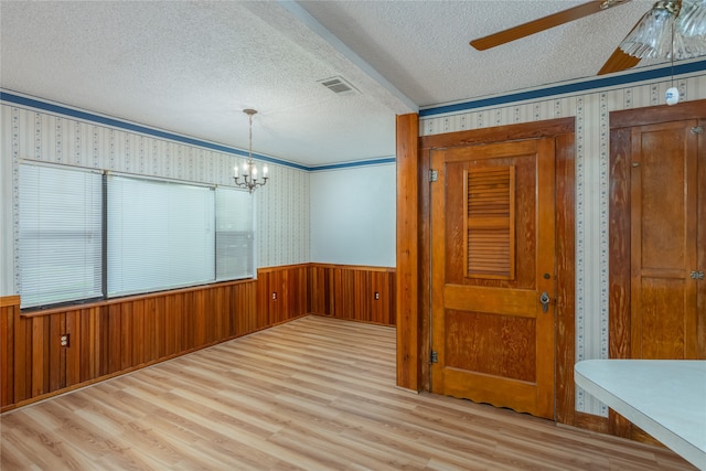 unfurnished room with ceiling fan with notable chandelier, a textured ceiling, wood walls, and light hardwood / wood-style floors