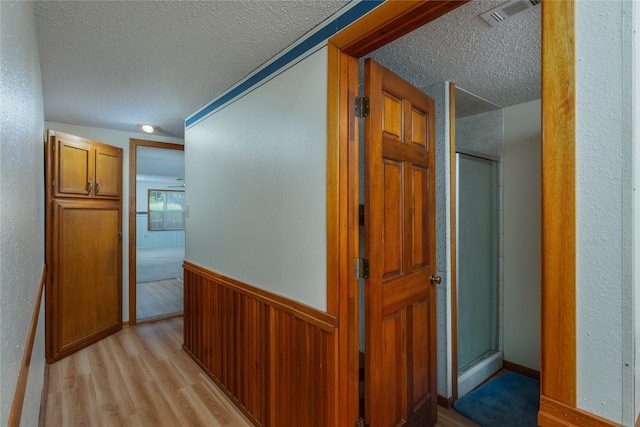 hall with light wood-type flooring, wooden walls, and a textured ceiling