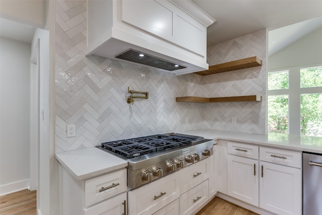 kitchen with light wood-type flooring, white cabinets, stainless steel appliances, and tasteful backsplash