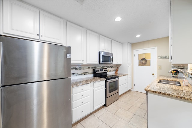 kitchen featuring appliances with stainless steel finishes, white cabinetry, sink, and light stone countertops