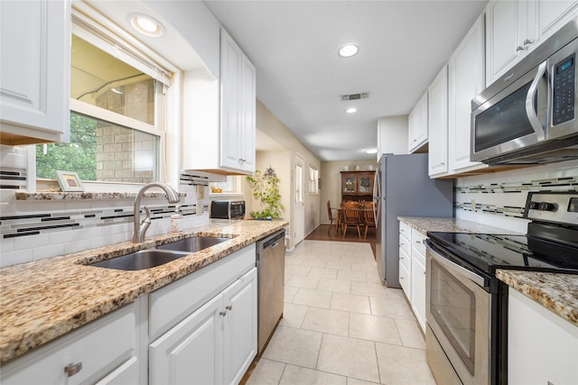 kitchen with light stone counters, stainless steel appliances, sink, and white cabinetry