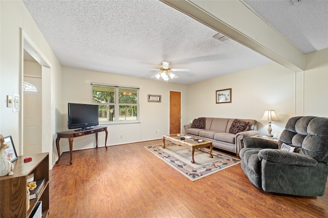 living room with wood-type flooring, beam ceiling, a textured ceiling, and ceiling fan