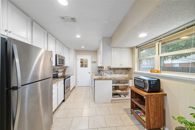 kitchen with light tile patterned floors, stainless steel appliances, sink, light stone counters, and white cabinets