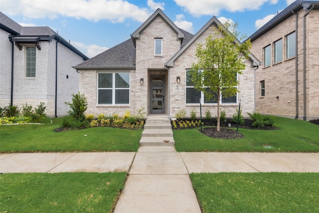 view of front of property featuring a shingled roof, a front yard, and brick siding