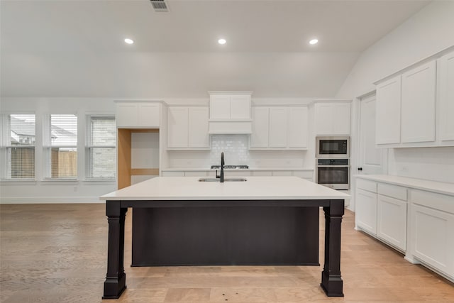 kitchen with light hardwood / wood-style floors, a kitchen island with sink, appliances with stainless steel finishes, and vaulted ceiling