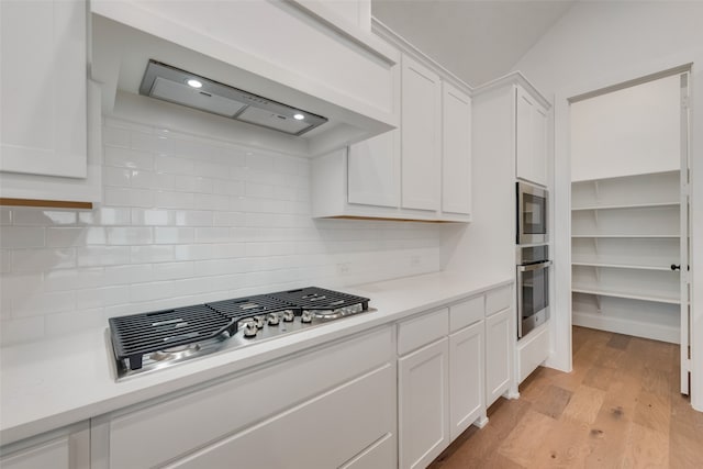 kitchen with white cabinets, light wood-type flooring, stainless steel appliances, and backsplash