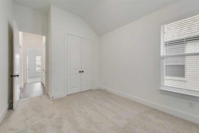 unfurnished bedroom with light colored carpet, a closet, and vaulted ceiling