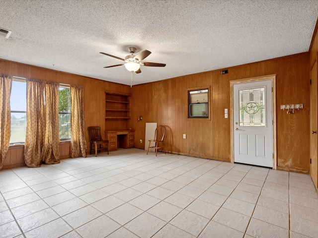 empty room with wood walls, ceiling fan, light tile patterned floors, and a textured ceiling