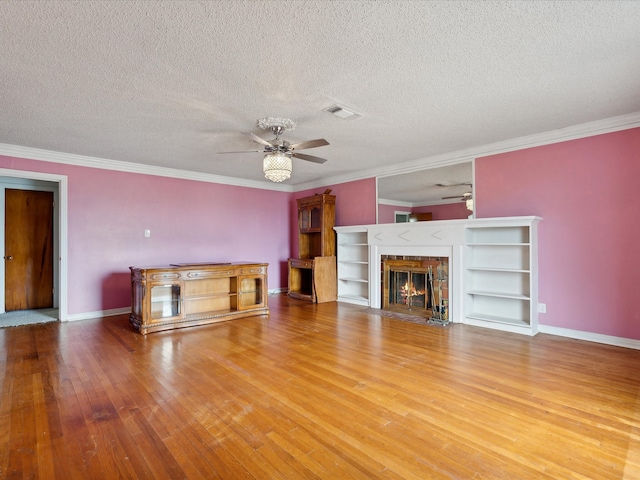 unfurnished living room with a textured ceiling, a fireplace, wood-type flooring, ornamental molding, and ceiling fan