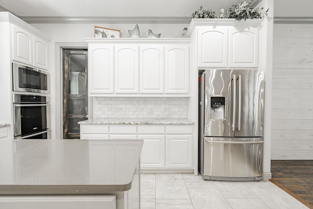 kitchen featuring crown molding, stainless steel appliances, white cabinetry, light stone counters, and light wood-type flooring