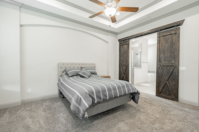 bedroom with ensuite bath, a barn door, a raised ceiling, carpet floors, and ceiling fan