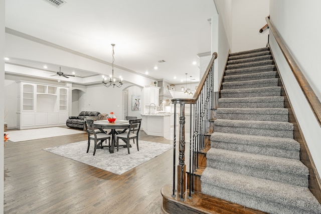 stairway featuring ceiling fan with notable chandelier, crown molding, wood-type flooring, and sink