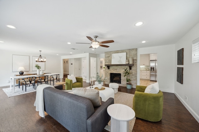 living room with ceiling fan with notable chandelier, dark hardwood / wood-style floors, and a stone fireplace