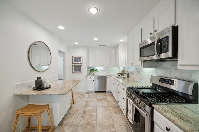 kitchen featuring white cabinetry, sink, light stone counters, a breakfast bar area, and appliances with stainless steel finishes