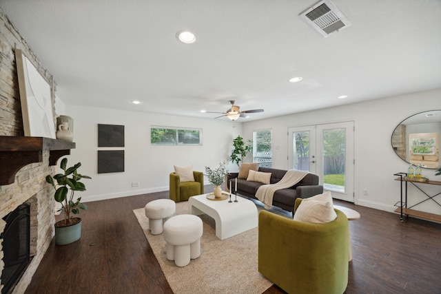 living room with ceiling fan, a stone fireplace, dark wood-type flooring, and a wealth of natural light