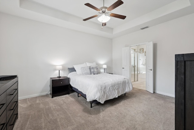 carpeted bedroom with ceiling fan, ensuite bath, and a tray ceiling