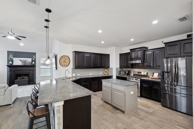 kitchen with light hardwood / wood-style flooring, stainless steel appliances, kitchen peninsula, ceiling fan, and a breakfast bar