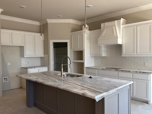 kitchen featuring custom exhaust hood, white cabinets, sink, an island with sink, and decorative light fixtures