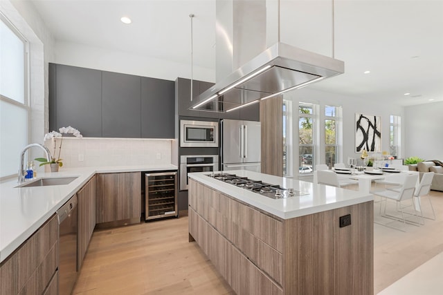 kitchen with light wood-type flooring, stainless steel appliances, sink, beverage cooler, and island range hood