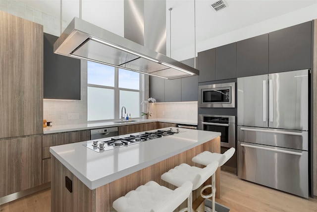 kitchen with light wood-type flooring, stainless steel appliances, a center island, wall chimney exhaust hood, and a breakfast bar area