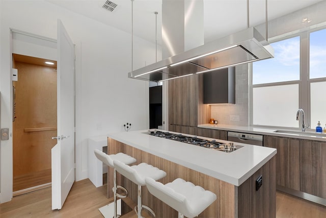 kitchen featuring hanging light fixtures, light hardwood / wood-style floors, sink, island exhaust hood, and a breakfast bar