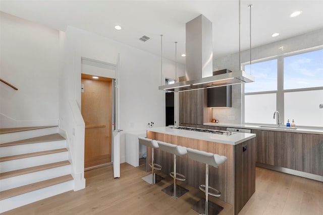 kitchen with decorative light fixtures, light hardwood / wood-style floors, island exhaust hood, a breakfast bar, and sink