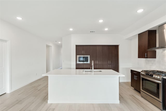 kitchen featuring a kitchen island with sink, sink, built in microwave, and stainless steel gas range